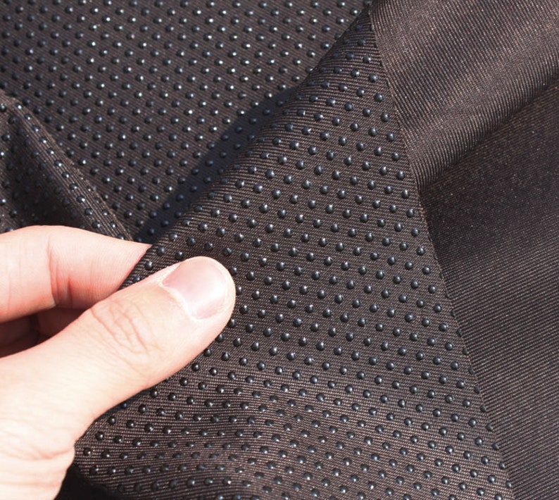 May include: Close-up of brown fabric with a textured pattern of small black dots. The fabric is folded over, showing the underside of the material.