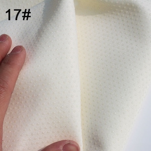 May include: Close-up of a white fabric with a textured surface. The fabric has a subtle pattern of small dots. The fabric is folded in half, and the edge of the fold is visible. The fabric is labeled "17#"