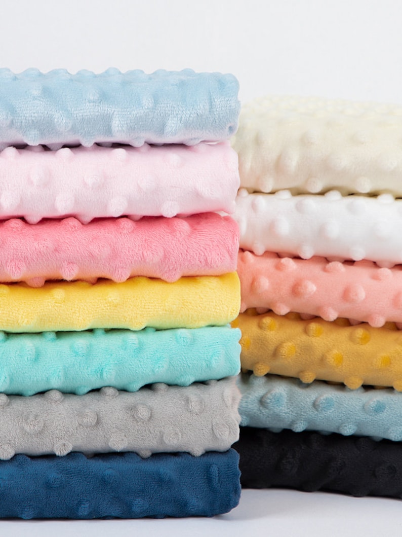May include: A stack of 10 different colours of soft, plush fabric with a textured, dotted surface. The fabric is folded neatly and arranged in a rainbow pattern.