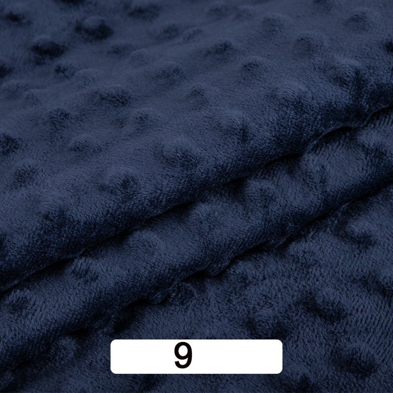 May include: Close-up of a dark blue fabric with a textured, bumpy surface. The fabric is folded over itself, creating a layered effect. The number "9" is printed on a white label in the lower centre of the image.