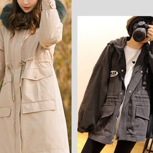 May include: Two women wearing long, hooded jackets. The jacket on the left is beige with a fur trim around the hood. The jacket on the right is black with a drawstring waist and a patch on the left sleeve that says "REAL".