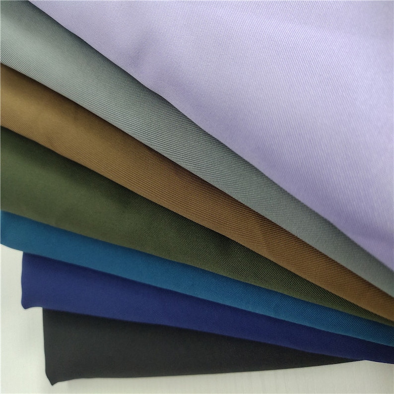 May include: A stack of six fabric swatches in different colors, including light purple, gray, brown, green, blue, and black. The fabric has a subtle texture.