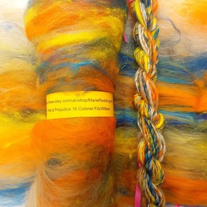 Puede incluir: Un ovillo de hilo teñido a mano en tonos de naranja, amarillo, azul y verde. El hilo está trenzado y atado con una cinta rosa. La etiqueta dice "Pride & Prejudice 16 Colonel Fitzwilliam" y "www.etsy.com/uk/shop/MarieReddingha".