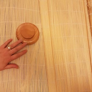 Könnte beinhalten: Eine hellfarbene Sushi-Rolle aus Bambus mit einem Holzdeckel. Die Matte besteht aus dünnen, parallelen Bambusstreifen, die durch Fäden zusammengehalten werden. Der Deckel ist rund und aus Holz.