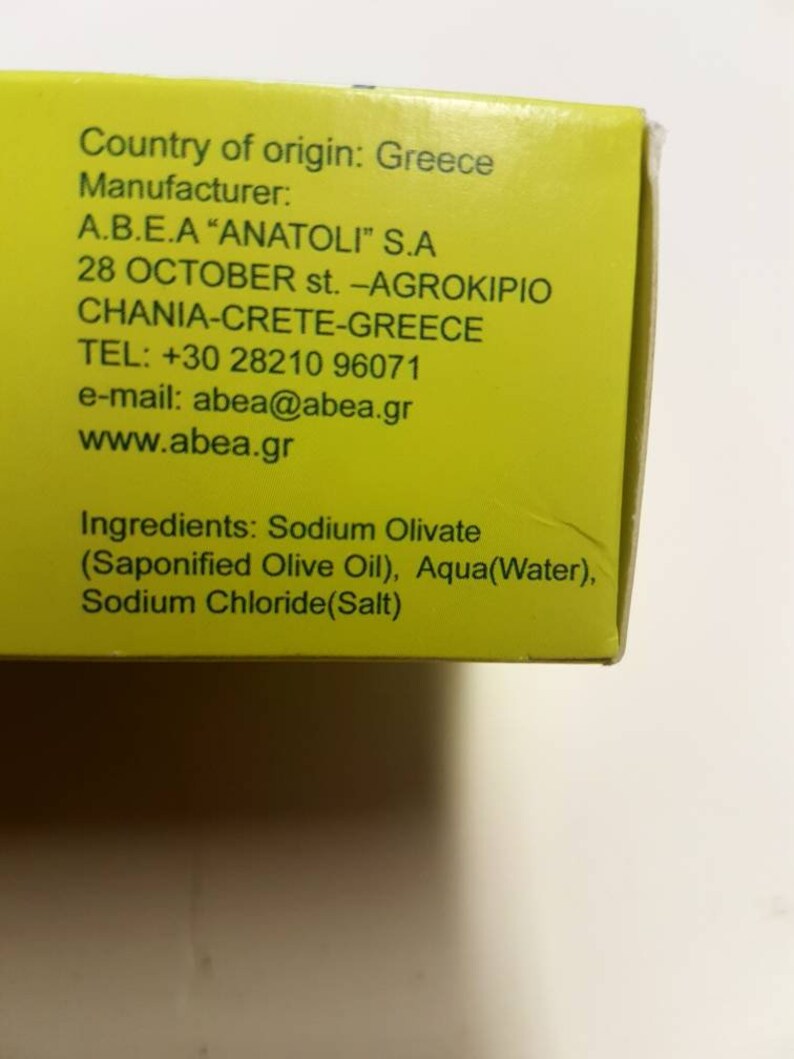 May include: A yellow box with black text listing the country of origin, manufacturer, address, phone number, email address, website, and ingredients for a product. The text reads: Country of origin: Greece Manufacturer: A.B.E.A "ANATOLI" S.A 28 OCTOBER st. -AGROK&Iota;&Rho;&Iota;&Omicron; CHANIA-CRETE-GREECE TEL: +30 28210 96071 e-mail: abea@abea.gr www.abea.gr Ingredients: Sodium Olivate (Saponified Olive Oil), Aqua (Water), Sodium Chloride(Salt)