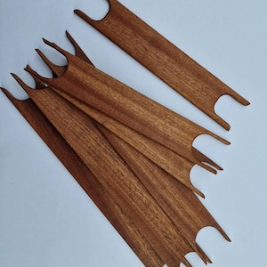 May include: Six wooden weaving needles with a reddish-brown finish. The needles are arranged in a fan shape, with the tips of the needles pointing towards the bottom of the image.