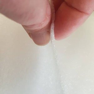 Pode incluir: Um close-up de um tecido branco, el&aacute;stico, sendo puxado para fora, revelando as fibras dentro.