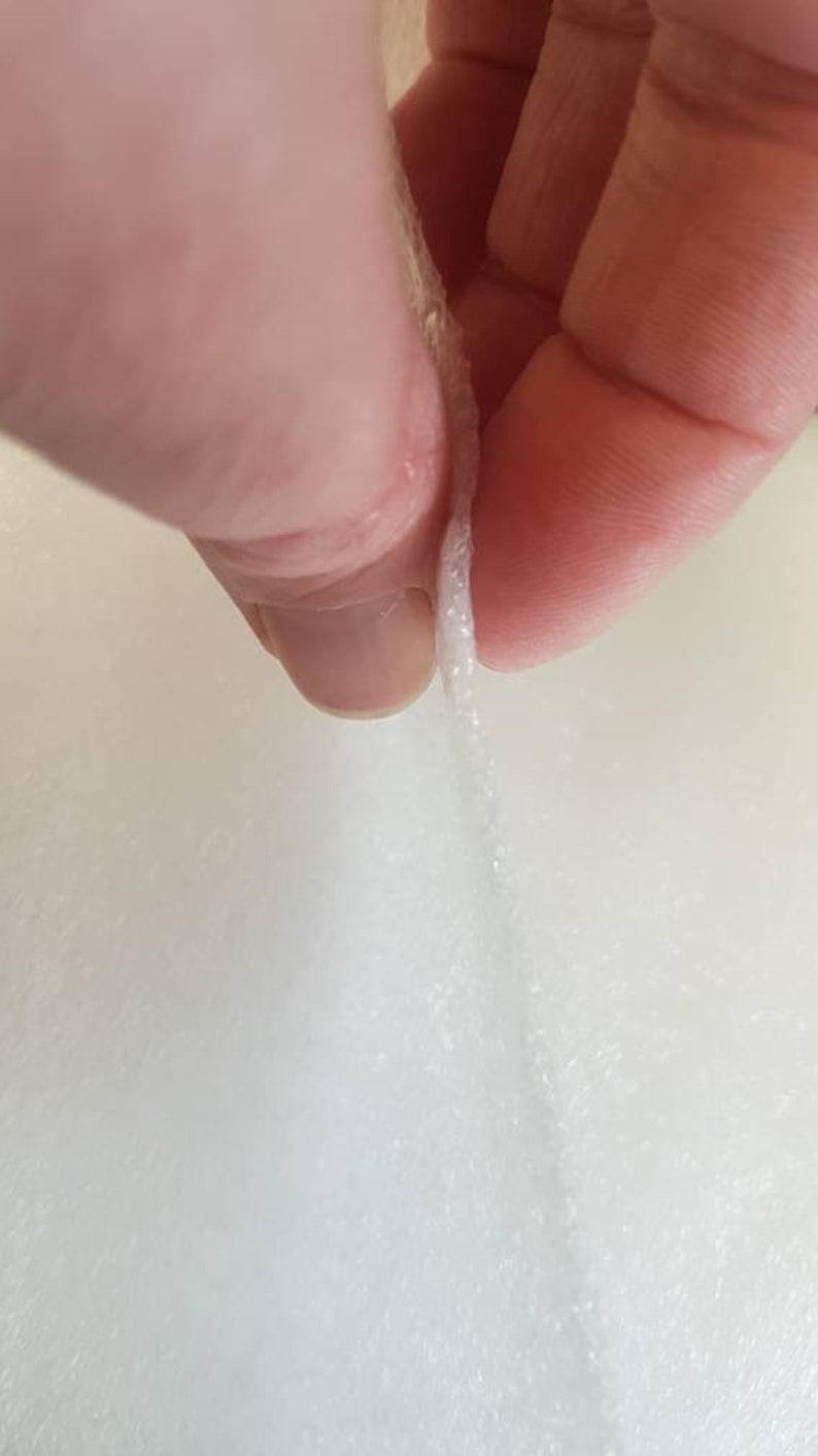 Pode incluir: Um close-up de um tecido branco, el&aacute;stico, sendo puxado para fora, revelando as fibras dentro.