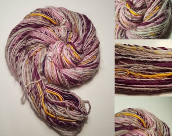 May include: A skein of hand-dyed yarn in shades of pink, purple, white, and yellow. The yarn is made of wool and silk and has a soft, fuzzy texture.