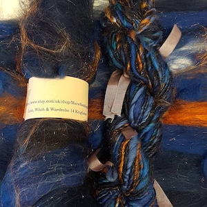 Op de afbeelding: Een bundel blauwe, oranje en zwarte garen met een label met de tekst "www.etsy.com/uk/shop/MarieRedding Lion, Witch & Wardrobe 14 Kingfisher"