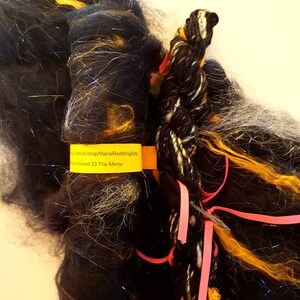 May include: A bundle of yarn in black, gold, and white with a pink ribbon. The yarn is labelled "Advent 23 The Mirror".