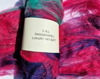 May include: A bundle of colorful art batt fiber in shades of teal, magenta, and purple. The fiber is wrapped with a label that reads "3 Jill Daggerspell Luxury Art Batt."