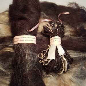 May include: Two skeins of brown wool yarn, one with a white and brown variegated yarn. The skeins are tied together with a pink ribbon. The text on the ribbon reads "www.etsy.com/uk/shop/MarieRedding Delights Advent 4 The Wolves Are B shop Marie Reds The Wolves Ann"