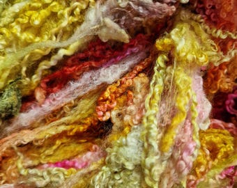 May include: Close-up of colorful, textured yarn in shades of yellow, orange, pink, and red. The yarn has a curly, fluffy appearance, suggesting it's suitable for crafting projects like knitting or weaving. The vibrant colors create a warm and inviting aesthetic.