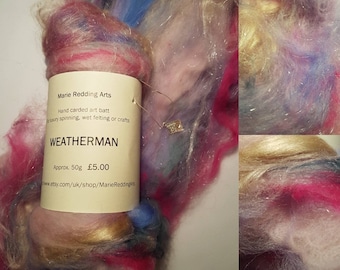May include: A hand-carded art batt in shades of pink, blue, purple, and gold. The label reads "Marie Redding Arts" and "WEATHERMAN" with a price of $5.00 for approximately 50 grams.