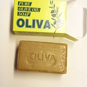May include: A yellow box with green text and an olive branch design reads "PURE OLIVE OIL SOAP OLIVA". The box is open and a brown bar of soap with the word "OLIVA" embossed on it is visible.
