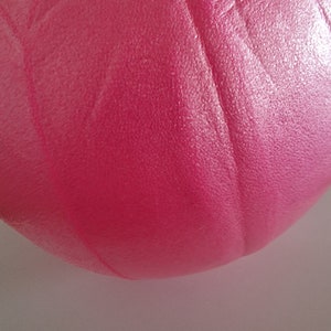 May include: A close-up of a pink exercise ball. The ball is made of a textured material and has a slight sheen.
