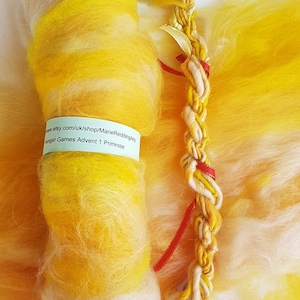 May include: A roll of yellow and white wool yarn with a red and white braided cord. The yarn is labeled "Hunger Games Advent 1 Primrose".