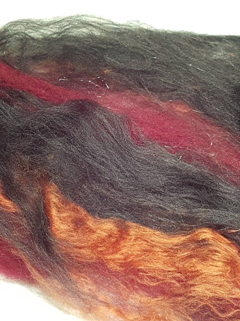 Op de afbeelding: Een close-up van een bundel garen in de kleuren zwart, bordeauxrood en oranje. Het garen is zacht en pluizig, en perfect om te breien of te haken.