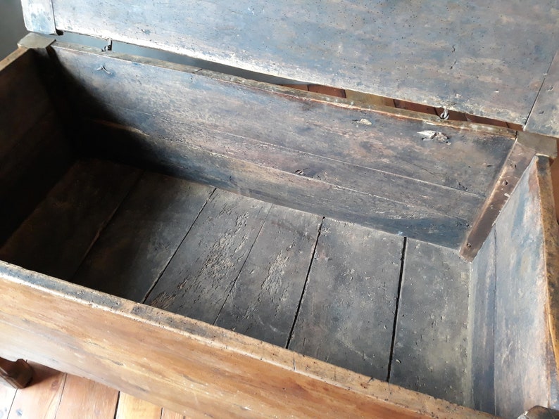 May include: An antique wooden chest with a hinged lid, open to reveal the empty interior. The chest is made of dark wood with a natural finish and has a simple design.