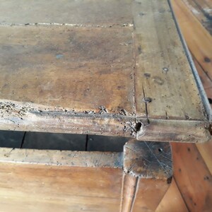 May include: Close-up of the top edge of a wooden chest with a drawer. The wood is a dark brown color and has a rough, worn texture. The chest has a simple design with a rectangular shape and a slightly rounded edge.
