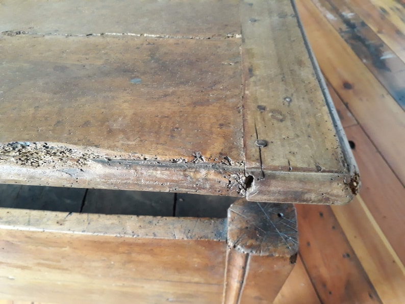 May include: Close-up of the top edge of a wooden chest with a drawer. The wood is a dark brown color and has a rough, worn texture. The chest has a simple design with a rectangular shape and a slightly rounded edge.