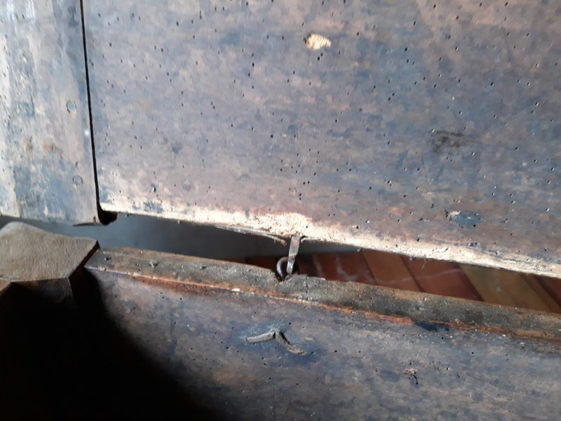 May include: A wooden box with a hinged lid and a metal latch. The box is made of dark wood and has a worn, rustic appearance. The lid is open, revealing the interior of the box.