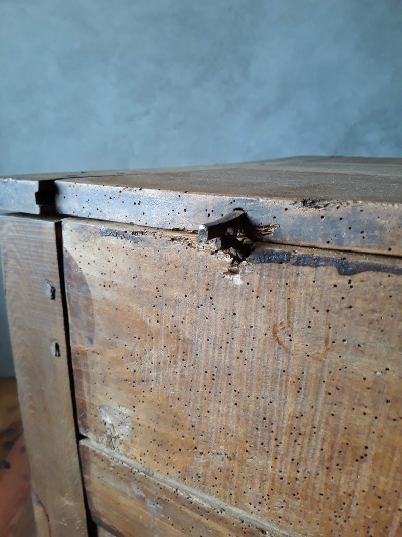 May include: A wooden chest with a hinged lid and a metal latch. The chest is made of dark wood and has a distressed finish. The chest is covered in small holes, possibly from insect damage.