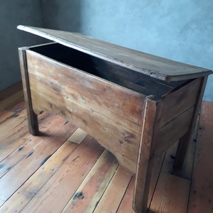 May include: A vintage wooden storage chest with a hinged lid, open to reveal the empty interior. The chest is made of natural wood with a rustic finish and sits on a wooden floor.