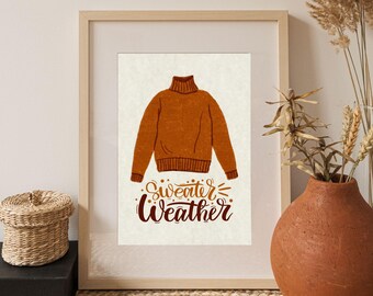 May include: A framed print with a brown turtleneck sweater illustration and the text "sweater weather" in a brown and gold script font.