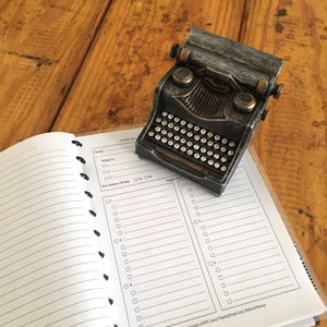 May include: A black and silver vintage-style typewriter on a white planner with a checklist for writing a book. The planner has sections for "Concept", "Writing For", "Have Audience Already", and "Chapter Ideas".