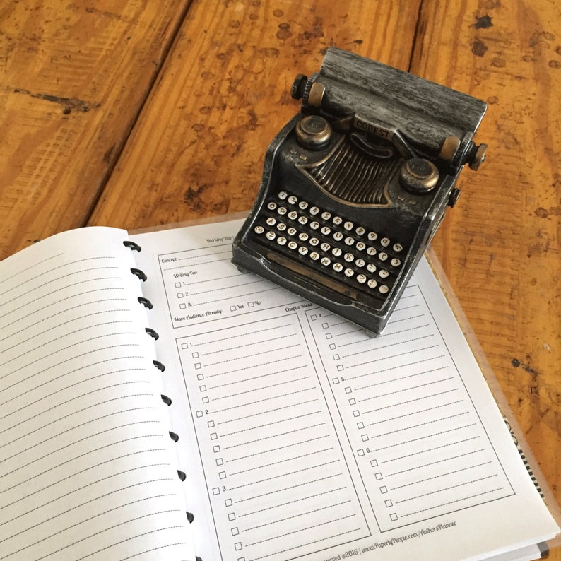 May include: A black and silver vintage-style typewriter on a white planner with a checklist for writing a book. The planner has sections for "Concept", "Writing For", "Have Audience Already", and "Chapter Ideas".