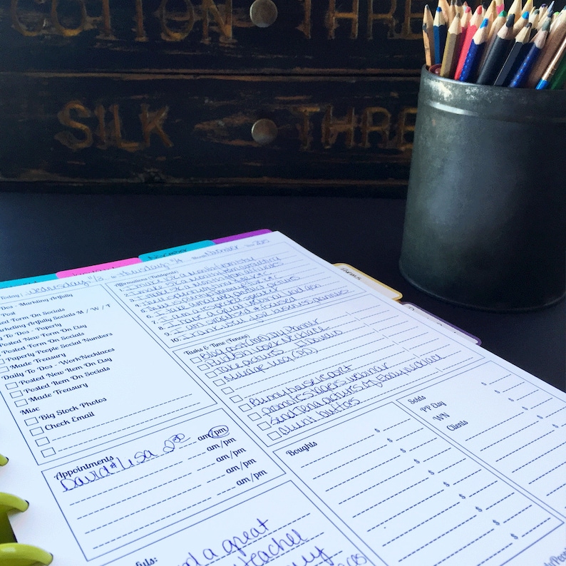 May include: A close-up of a white planner with blue ink. The planner has a tabbed section for each day of the week. The planner is open to Wednesday, August 16th. The planner has a section for appointments, to-do list, and notes. The planner is sitting on a black surface with a black tin filled with colored pencils.