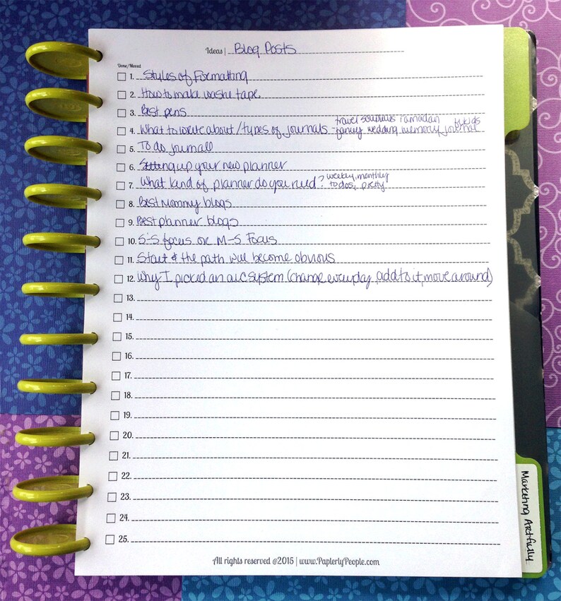 May include: A white notepad with a list of blog post ideas, including topics like formatting and journals. The notepad is bound with yellow plastic rings and sits on a patterned background.