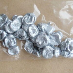 May include: A close-up of a plastic bag filled with small, silver, metallic, irregularly shaped pieces. The pieces are smooth and shiny.