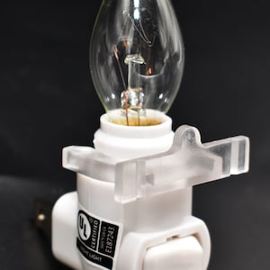 May include: White plastic night light with a clear light bulb and an on/off switch. The light has a UL Certified label with the number E187243.