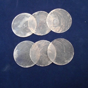 May include: Six iridescent white mother of pearl shell discs, arranged in two rows of three, on a dark blue background.