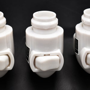 May include: Three white plastic light switch adapters with a rocker switch on the side. The switches are in the off position.