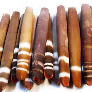 May include: A collection of approximately 20 banded agate stones, each with a unique pattern of brown, white, and black stripes. The stones are smooth and polished, and they are arranged in a row.