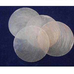 May include: A collection of five iridescent, circular shell pieces. The shells have a pearlescent sheen and a slightly textured surface. They are arranged on a dark blue background, creating a contrast that highlights their natural beauty.
