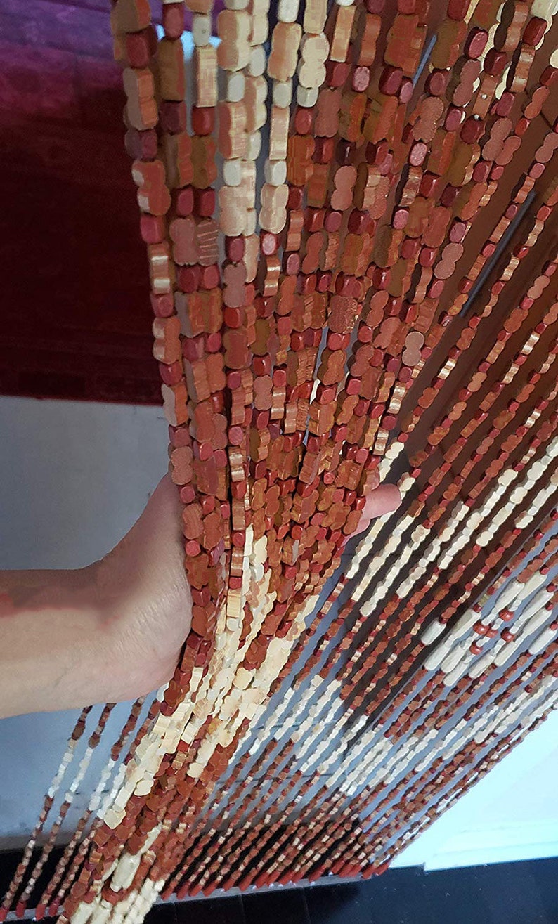 May include: A wooden beaded curtain with alternating light brown and reddish-brown beads. The curtain is hanging from a doorway and is being held open by a hand.