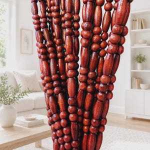 May include: A close-up of a beaded curtain made of dark reddish-brown wooden beads. The beads are various shapes and sizes, strung together to create a decorative curtain. The curtain hangs in front of a living room.