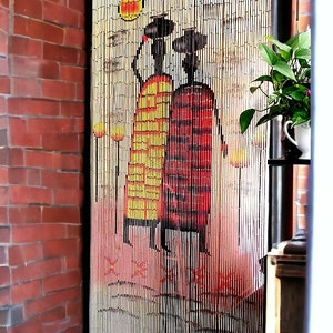 May include: Bamboo beaded curtain with a painted design of two figures in traditional dress. The figures are in yellow and red, with a sun and stylized trees. The curtain hangs in a doorway, next to a brick wall.