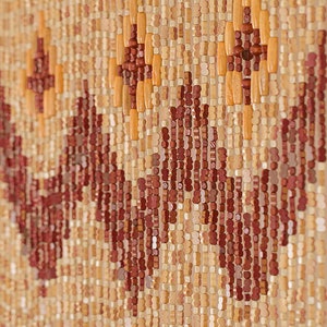 May include: A beaded curtain made of wood beads in shades of brown, beige, and orange. The beads are arranged in a geometric pattern, creating a unique and decorative design.