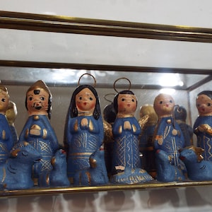 May include: A nativity scene set with 10 blue and gold painted figurines in a glass display case. The figures include Mary, Joseph, baby Jesus, three wise men, an angel, and a shepherd.