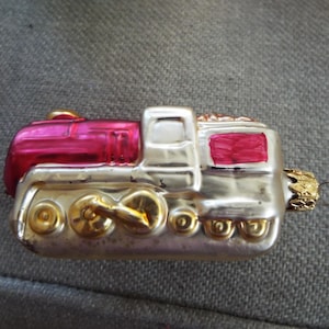 May include: A red and silver glass ornament shaped like a train engine. The engine has a red cab and a silver body with gold wheels. The ornament has a gold loop for hanging.