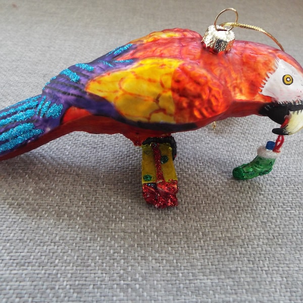 kurt adler hand painted blown glass parrot bird ornament  bird holding a sox perched on a present  red green gold   tail glitter paper label