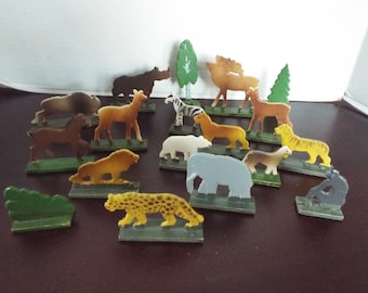 May include: A collection of vintage toy animal figurines, including a zebra, lion, tiger, elephant, and deer. The figurines are made of plastic and are various colors. There are also small green tree and bush figurines.