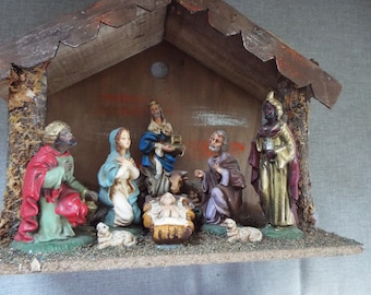 May include: A vintage wooden nativity scene featuring figurines of Mary, Joseph, baby Jesus, three wise men, and sheep. The scene is painted in muted colours and has a rustic look.
