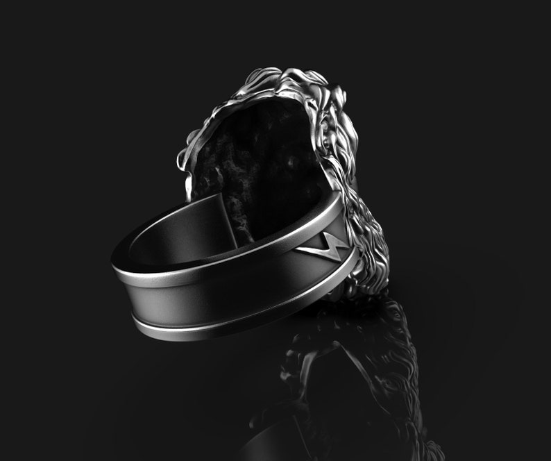 May include: A silver ring with a lion head design. The ring has a black band with a lightning bolt design.